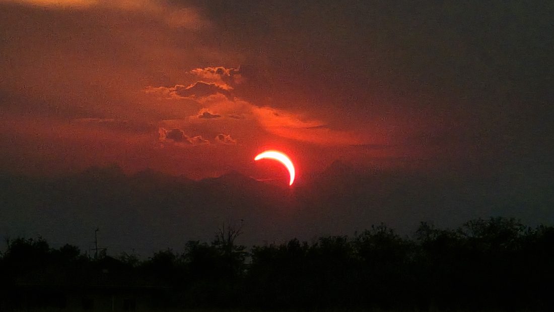 Cielo carico di nuvole al tramonto sopra il profilo delle Alpi, con la pioggia che scende in lontananza.